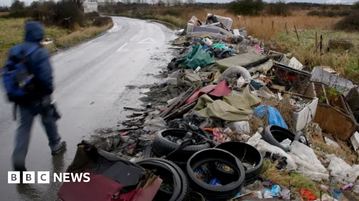 A man pictured walking on the footpath alongside huge amounts of rubbish which has been fly tipped.