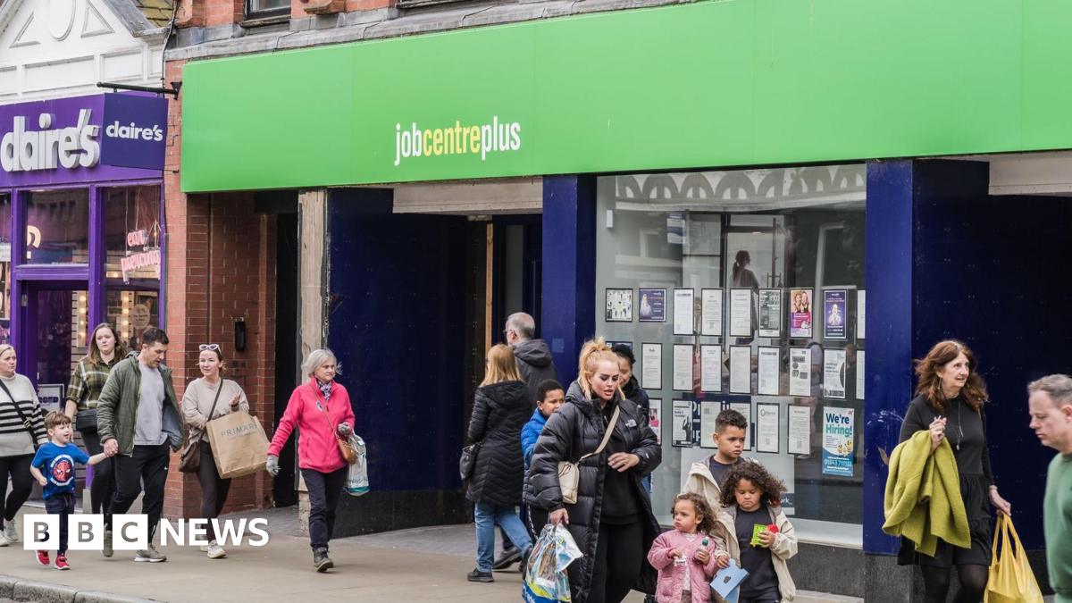 People, including families, walking on a street past the Job Centre Plus employment office in Chester. The street is busy, the weather is dry but people are wearing coats.
