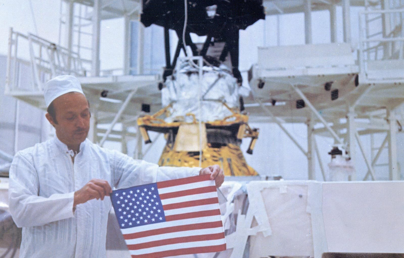 With Voyager 2 in the background, John Casani holds a small U.S. flag
