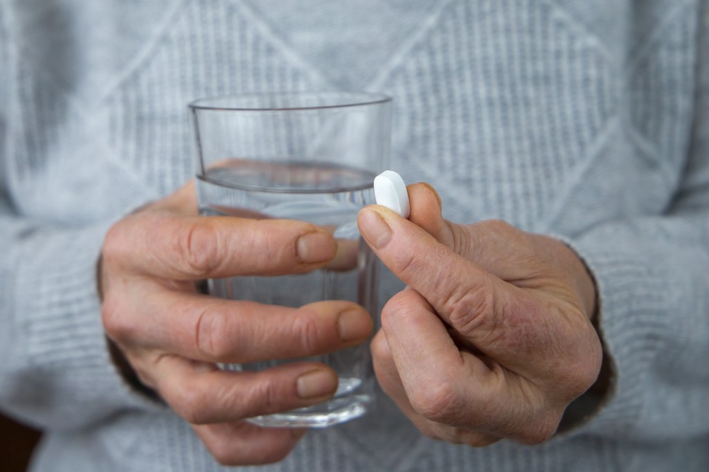 Close-up of an elderly woman's hands holding a pill and a glass of water.