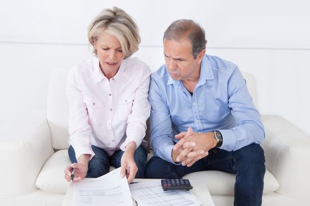 An older man and woman are sitting on a sofa looking at household bills 