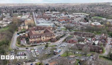 A drone-image of Nottingham City Hospital with city skyline in the background. Car parks and surrounding buildings can be seen in the aerial image