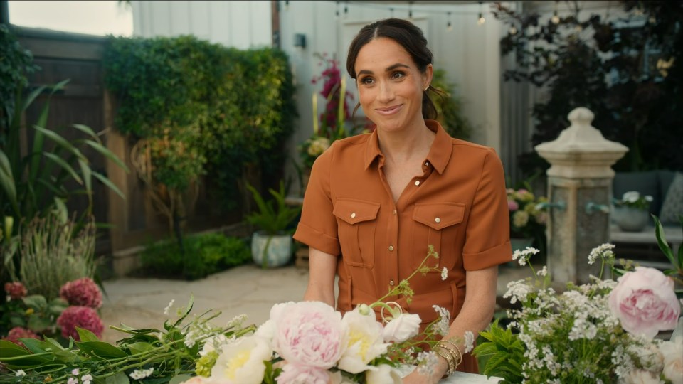 Meghan, Duchess of Sussex, in a rust-colored dress, arranging flowers.