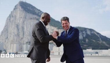 UK Foreign Secretary David Lammy and Chief Minister of Gibraltar Fabian Picardo clasp hands laughing, as they stand in front of the rock of Gibraltar.