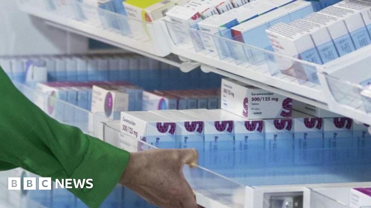 A photo of a hand in a green shirt pulling out a drawer in a pharmacy.