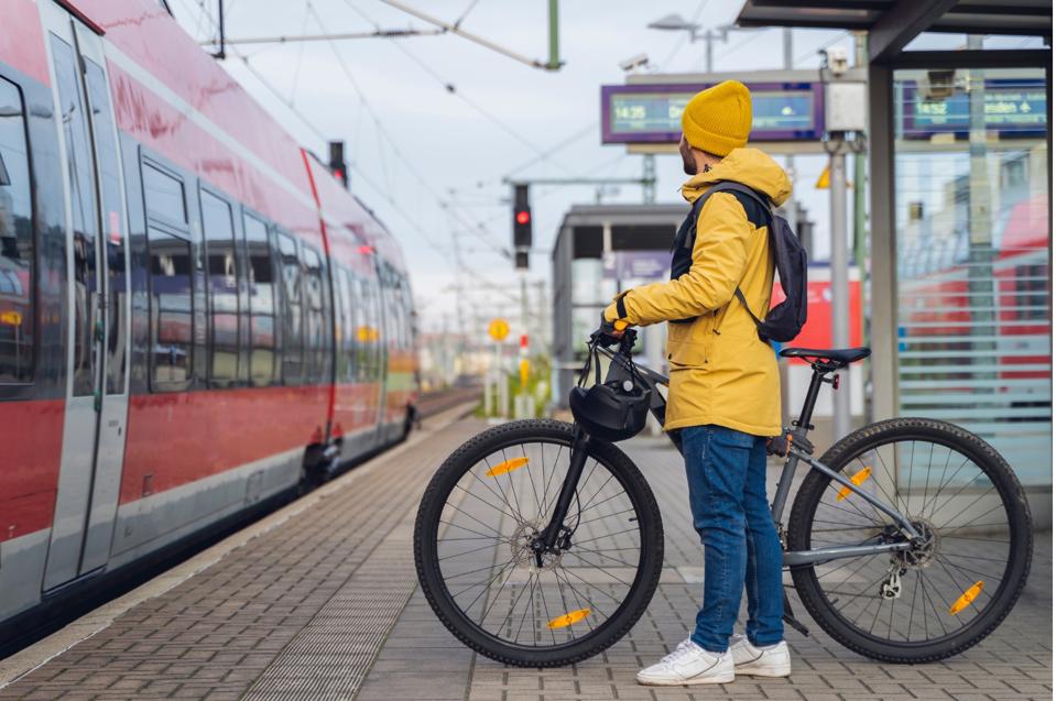 A photo of a cyclist about to board a train with his bicycle in tow.