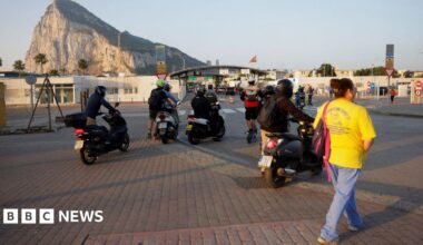 People on foot and motorbikes cross the border from Spain to Gibraltar at dawn, in front of the Rock