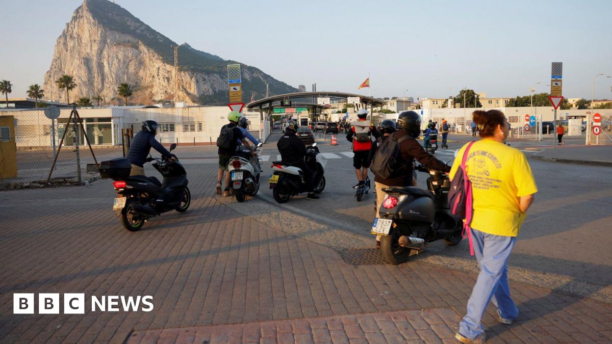 People on foot and motorbikes cross the border from Spain to Gibraltar at dawn, in front of the Rock
