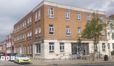 The corner view of a building - it is red brick on top and white brick on the bottom. A police car is at the side of the building.