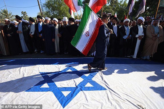 TOPSHOT - An Iraqi man steps on a flag of Israel during a march in the Kadhimiya district of Baghdad on June 21, 2025, to protest against Israel's strikes on Iran. (Photo by AHMAD AL-RUBAYE / AFP) (Photo by AHMAD AL-RUBAYE/AFP via Getty Images)