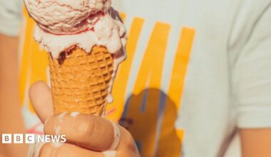 A hand holding an ice cream cone. The ice cream is melting onto the person's hand.
