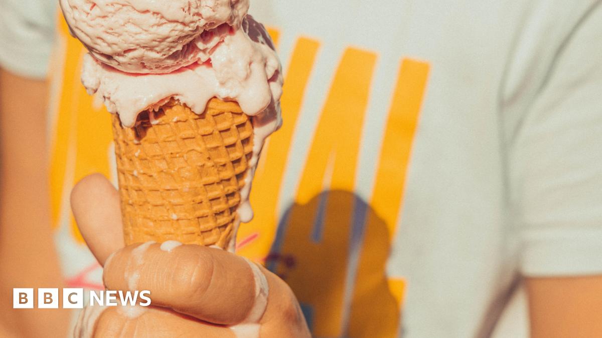 A hand holding an ice cream cone. The ice cream is melting onto the person's hand.