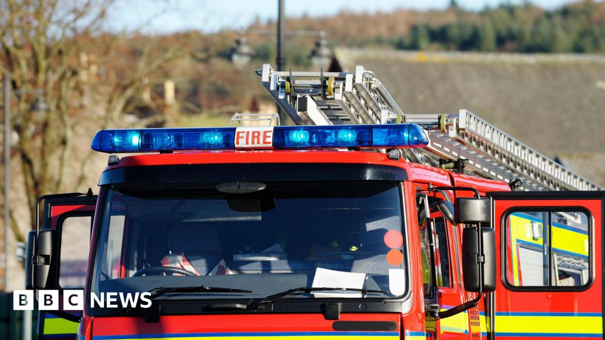 The top half of a red fire engine. The vehicle is red with high visibility stripes. There are blue lights on the top along with ladders. Doors on both sides are open. The front of the vehicle is empty.