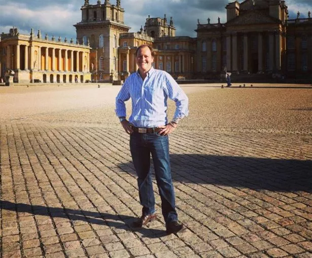 A man in a blue shirt and trousers, smiling in a grand courtyard