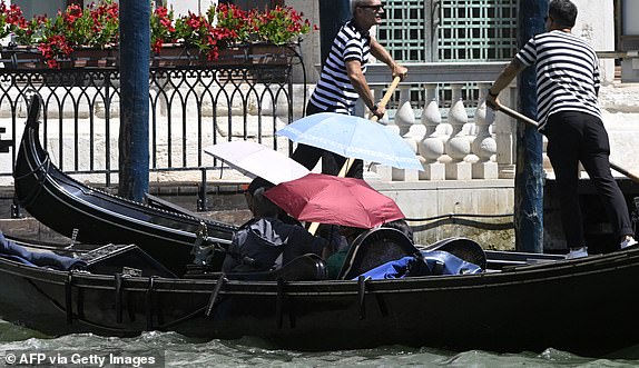 Tourists protect themselves from the sun with umbrellas during a gondola ride in Venice lagoon on June 27, 2025. Italy's health ministry warned residents and tourists on June 27, 2025 of soaring temperatures across the country, issuing a red alert for 21 cities this weekend. The ministry issued its top red alert for cities including the capital Rome, economic powerhouse Milan and Venice -- where the rich and famous are celebrating the wedding of Amazon tycoon Jeff Bezos. (Photo by ANDREA PATTARO / AFP) (Photo by ANDREA PATTARO/AFP via Getty Images)