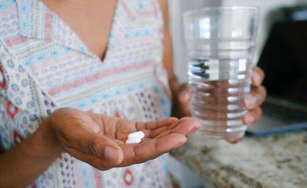 A close-up image of a woman in a kitchen taking medication