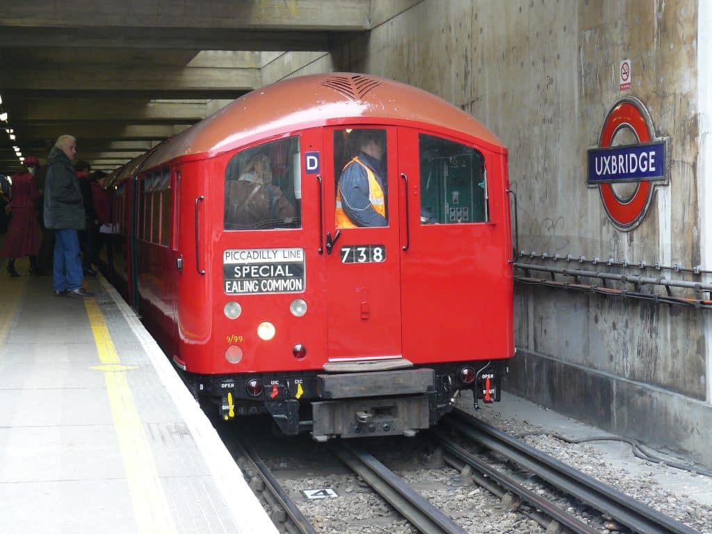 an Art Deco train travelling along the tracks, with the train driver visible through the window wearing a hi-vis