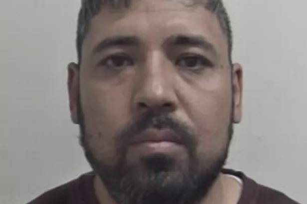 Custody image of Habib Behsodi who has short black hair and a beard and is wearing a burgundy top 