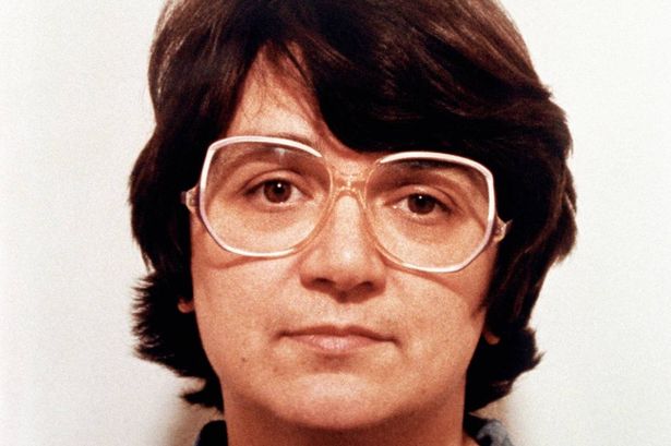 An old police mugshot of a woman with short hair and large glasses