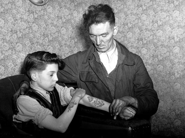 14-year-old Arthur Waterworth of Droylsden shows off his tattooed forearms to his father. January 13, 1956