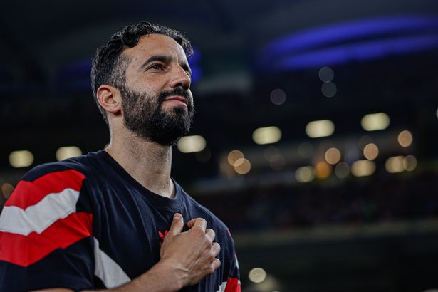 Ruben Amorim puts his hand on the Manchester United crest with a slight smile