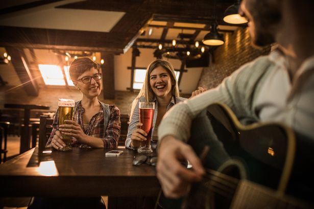 Cheerful female friends having fun while drinking beer and listening to their male friend playing acoustic guitar.