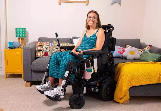 Emma Bray photographed in her wheelchair wearing a blue dress in front of a sofa