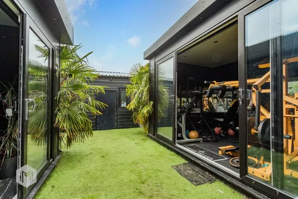 Black outbuildings in garden with one containing gym equipment
