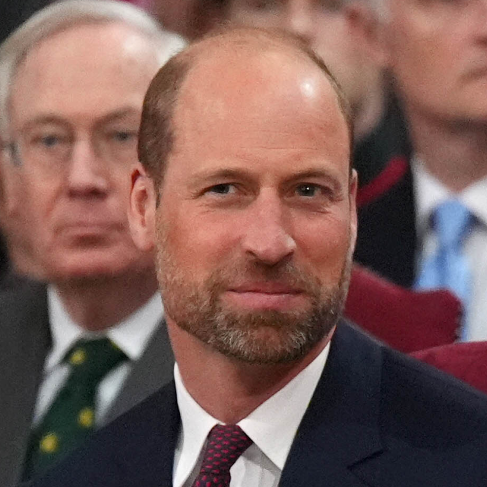  Prince William has a beard and a bald head and is smiling while wearing a navy suit and tie. 
