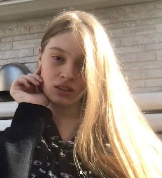 Person with long hair holding their face, wearing a patterned top, posing for a selfie outdoors