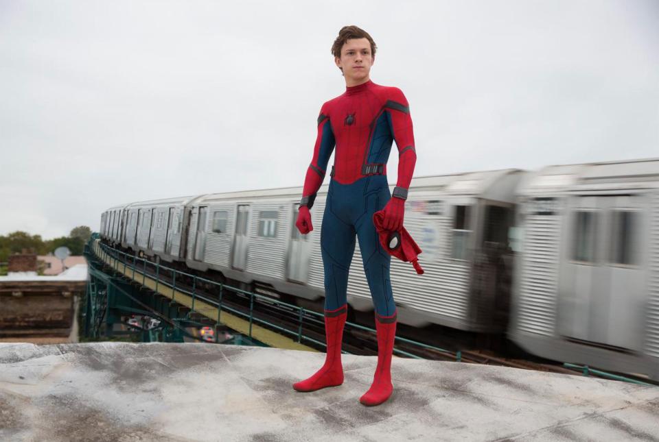 Spider-Man standing on a platform with a train in motion behind him.
