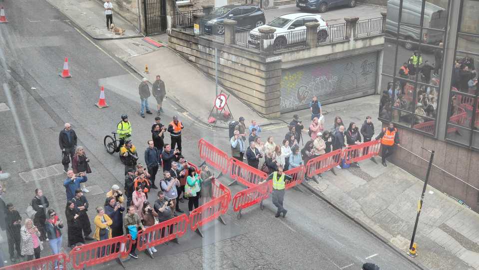 Aerial view of a crowd of people behind barriers on a city street.