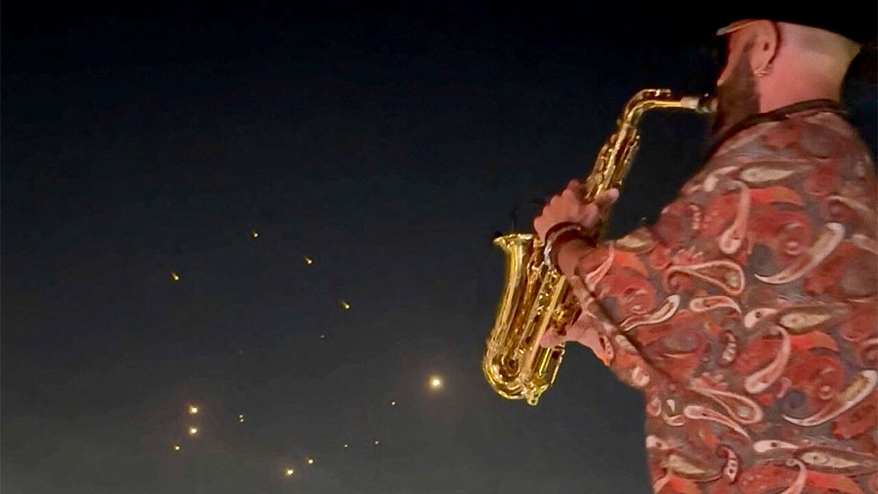 People record the missiles using their phones while a saxophonist plays the instrument, in Kfar Yassine