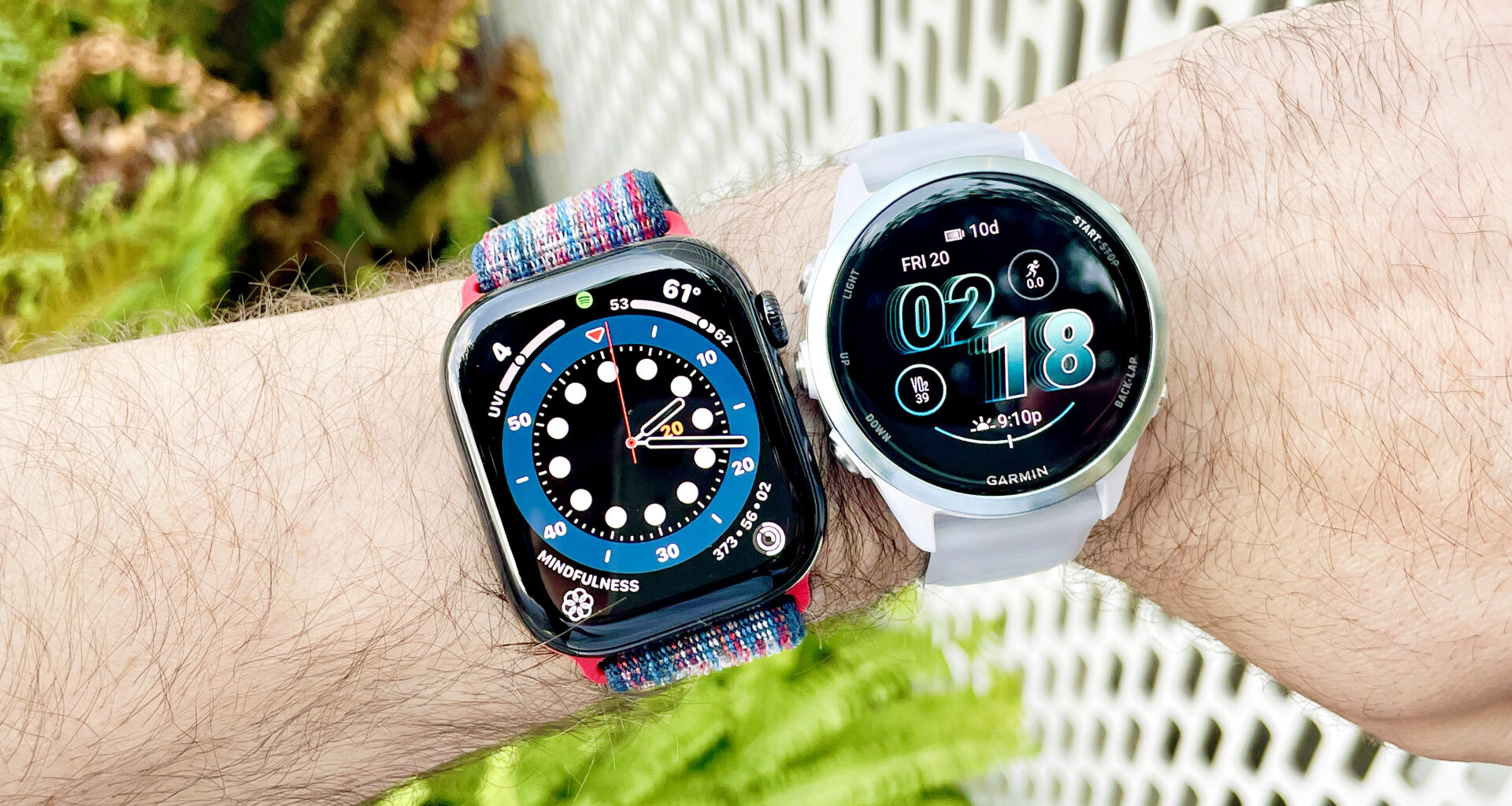 Apple Watch Series 10 next to a Garmin Forerunner 570 on a user's wrist with green foliage out of focus in the background