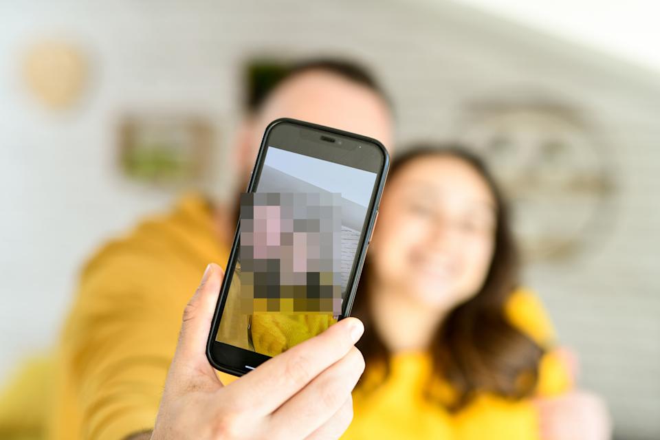 A couple takes a smiling selfie with a smartphone, capturing their faces in a cozy indoor setting