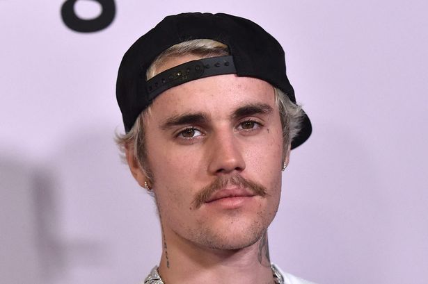Justin Bieber in a white top, silver chain and black baseball hat.