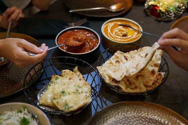 A delicious and comforting scene showcasing an Indian meal with butter chicken and naan. The rich and creamy butter chicken is served in a bowl with a smooth, thick gravy, garnished with cilantro. The naan, soft and slightly charred, is placed in a basket.