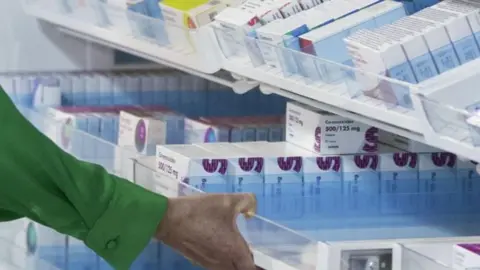 PA Media A photo of a hand in a green shirt pulling out a drawer in a pharmacy.