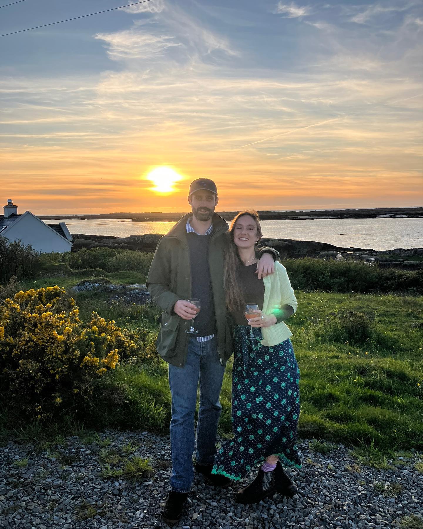 Lady Marina Windsor and Nico Macauley posing in front of the sea and a sunset