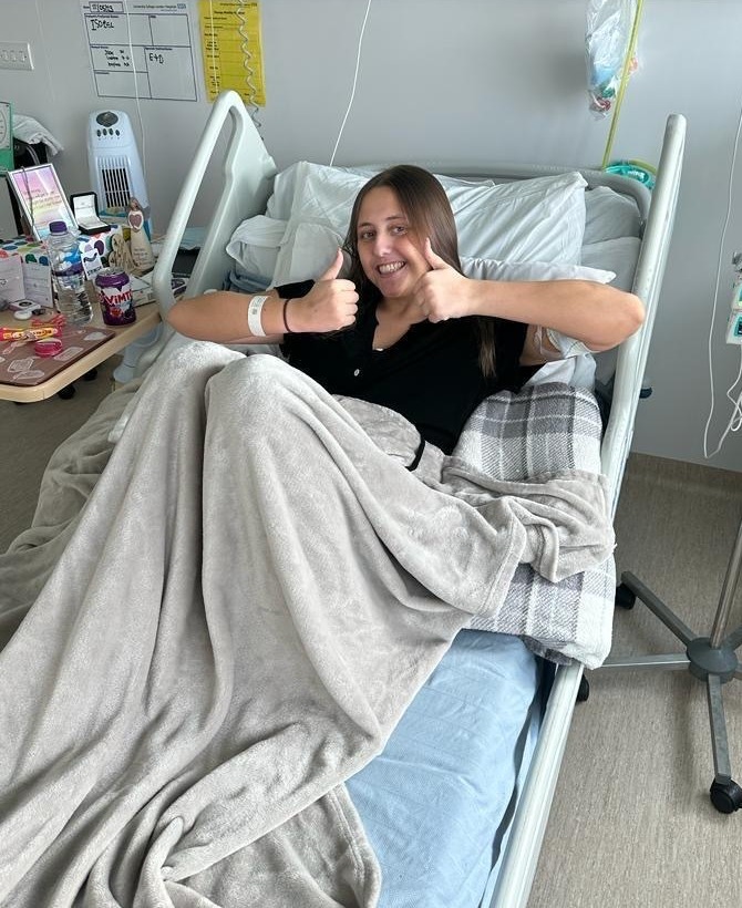 Woman in hospital bed giving thumbs up.