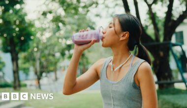 Young female athlete runner drinking protein shake after exercise workout in urban park.