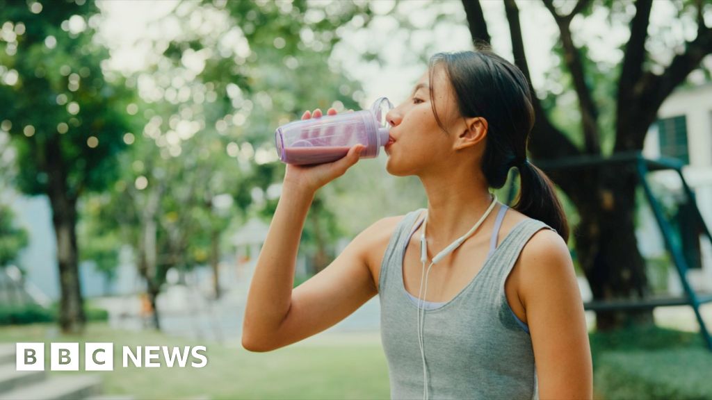 Young female athlete runner drinking protein shake after exercise workout in urban park.