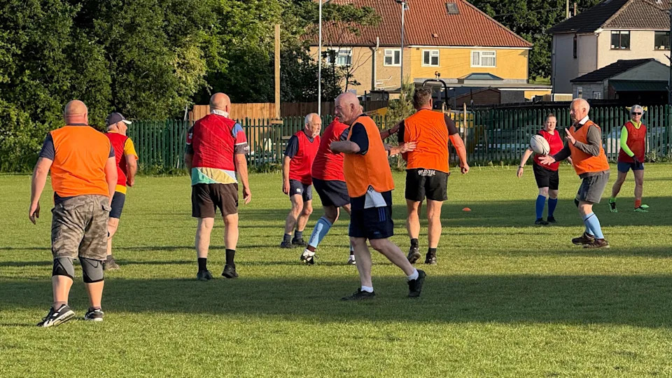 A group of mostly older people wearing orange and red bibs play walking rugby at Kingswood Rugby Club in Bristol