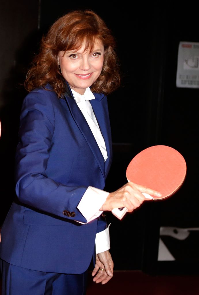 Susan Sarandon in a navy suit, smiling holding a ping pong racket