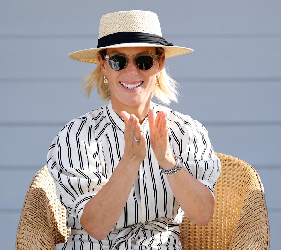 Zara Tindall wearing a white striped dress and straw hat clapping and smiling