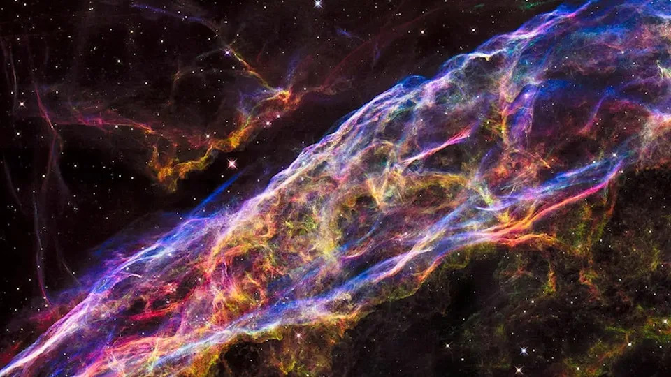  The remnants of a supernova explosion in outer space with rainbow swirling clouds. 