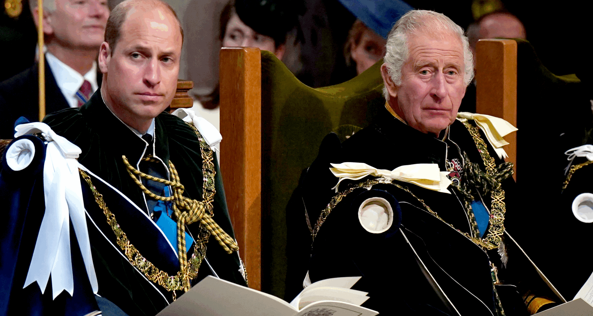 King Charles and Prince William wearing velvet robes sitting in chairs