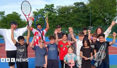 Photo of 15 people smiling and cheering on bright coloured tennis courts.