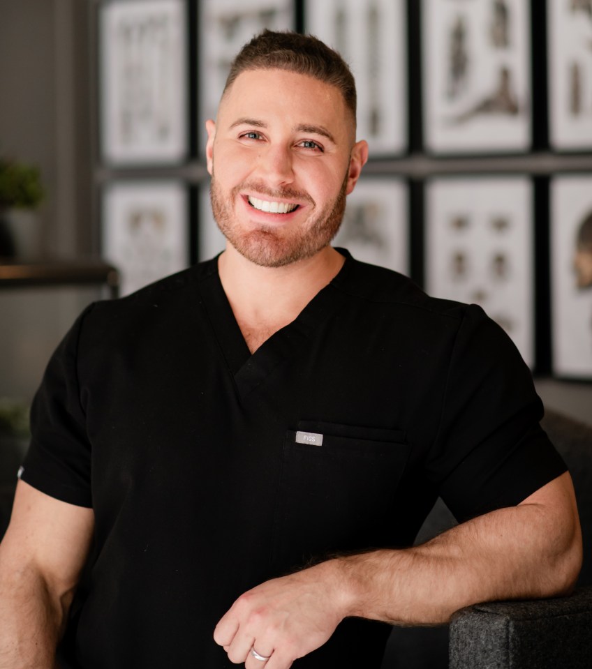 Portrait of a smiling man in a black scrub top.