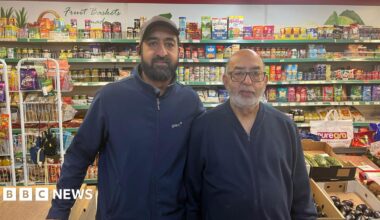 Two men, one on the right in his 60s, the one on the left in his 40s, standing in front of a shop